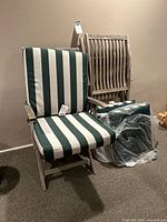 Two wooden folding outdoor chairs with slatted backrests and seats, one fully equipped with green and white striped cushions, the other without cushions, showing weathered finish.