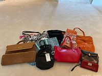 Overall group shot of nine handbags of various styles and colors arranged on floor.