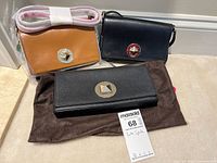 Three Kate Spade handbags displayed together with a MaxSold tag. The photo shows the black wallet clutch lying flat on a dark pouch, the tan crossbody handbag with a strap wrapped in white protective paper, and the navy blue small purse. Each has a circular gold-tone metal clasp with a pyramid stud in the middle and Kate Spade branding.