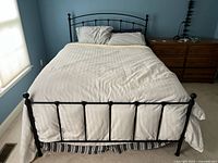 Full view of the queen size metal bed made up with white bedding and pillows, including striped bed skirt.