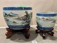 Photo of two blue and white ceramic planters with Asian landscape designs on carved wooden stands
