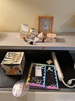 Overview of lot items on table including wooden boxes with animal motifs, figurines, seashells, two journals, and handheld lamp