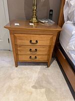 Front view of one nightstand showing three drawers and black metal handles