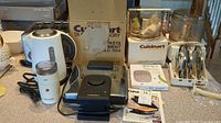 Kitchen counter setup with Cuisinart food processor, waffle iron, toaster, coffee grinder and coffee pot arranged, showing all main appliances in the lot
