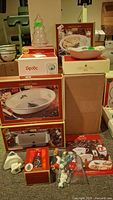 Photo showing boxed Spode Christmas Tree pattern dinnerware including pie dish, bowl, loaf pan, and additional items such as figurines and cheese cutters.