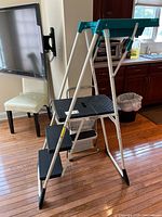 Step stool standing upright showing three black steps and white metal frame.