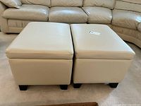 Two beige matching storage ottomans front view, showing smooth tops and short black legs.