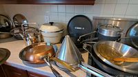 View of all cookware items arranged on countertop including copper fry pan, funnel, wok, teapot, and various pans.