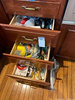 Three wooden drawers partially open showing a large collection of assorted cooking and food preparation utensils packed inside.