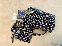 Photo showing full set of five Vera Bradley items on beige background, includes handbag and four smaller accessory pieces, all with floral or geometric patterns.