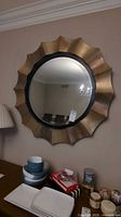 Front view of large round metal-look mirror with scalloped beveled edge frame hanging on wall, showing reflective surface and decorative frame.