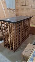 Side view of wood wine rack table showing lattice compartments for wine storage, flat dark wood tabletop surface, scuffs and stains visible.