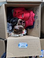 Box of assorted boy's clothing, shoes, and accessories including outerwear and hats from various brands.