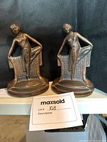 Pair of brass Art Deco dancer bookends shown side by side on a shelf with black background.