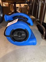 Side view of the B-Air blue air mover fan showing control panel with power switch and outlets, coiled electrical cord, and carrying handle.