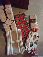 Assorted holiday and non-holiday linens and napkins, including Waterford and Crate and Barrel brands, with an autumn leaf patterned oven mitt and pumpkin shaped fabric item.