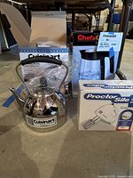 Photo showing the Cuisinart stainless steel whistling kettle, Chef's Choice electric glass kettle, and Proctor Silex hand mixer in boxes on floor.