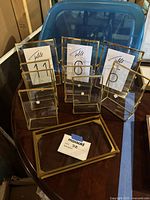 Set of glass and brass framed display boxes and picture frames arranged on a table with table number cards inside.