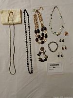 Full view of jewelry set laid out on white surface including 4 necklaces, 2 bracelets, 4 pairs of earrings, and 1 ring.
