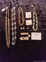 Photo showing all 10 jewelry pieces spread out on a dark fabric background: long necklaces in gold and silver tones, multicolored beaded necklace, earrings including Givenchy boxed studs, bracelets, rings, and a brooch.