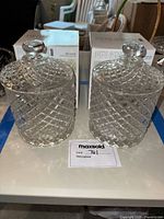 Two clear crystal jars with lids placed on a white surface, boxes of the same brand and model visible behind the jars.