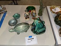 Lot overview showing ceramic turtle, frog, green rabbit vase, shell-shaped bowls, and two Hummel figurines