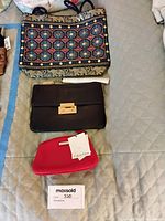 Four women's bags shown: a beaded floral tote, black clutch, red Calvin Klein cosmetic bag with tags, and brown Michael Kors leather handbag.