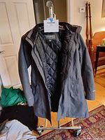 Photo of Eddie Bauer women's winter coat hanging on a stand showing the front with zipper open revealing the quilted lining inside and attached hood.