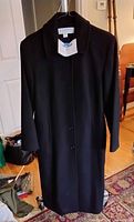 Photo of a black wool blend winter coat by Liz Claiborne, hanging with visible buttons and collar.