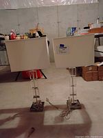 Two matching glass and silver-tone table lamps with white fabric rectangular shades side by side on floor.