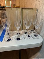 Eight clear Mikasa champagne flutes arranged on a table with original boxes behind them.