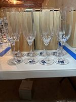 Eight clear Mikasa Stephanie champagne flutes arranged in a row with original cardboard boxes behind them.