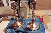 Pair of ornate pewter candlestick holders standing on a fabric surface with a blue cloth underneath.