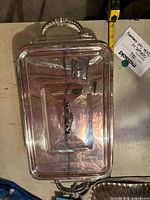 Top view of rectangular silver plated serving dish with ornate handle on the lid and tape measure showing approx 16 inch length.