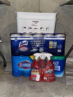 Full lot view showing three Resolve carpet spot remover bottles, two Lysol wipe packs, one Clorox wipe pack, two white plastic clothes hampers stacked behind wipes.