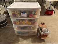 Photo of four white plastic drawers containing assorted ribbon spools and additional bin beside them with sewing threads and party supplies.