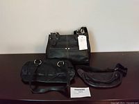 Three black leather or faux leather bags: handbag with tag, purse with rings, belt bag.