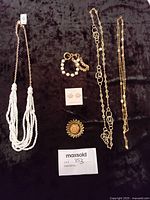 Photo of a jewelry set including three necklaces, a bracelet, a pair of earrings, and a brooch arranged on a dark fabric background with a Maxsold lot card.