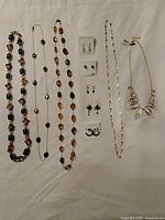 Photo showing an assortment of necklaces in mixed materials and colors, plus multiple pairs of earrings on brand cards, and chain style necklaces including those with tags.