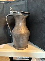 Full view of the pewter jug showing the body, handle, and hinged lid from one side.