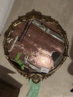 Front view of the oval mirror showing gold ornate frame and reflective surface.