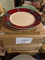 Stack of plates showing red tartan plaid design with gold and green accents on rim and plain center.