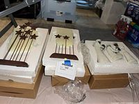 Photo showing two metal star backdrops and three Wisemen figurines in white styrofoam packaging on cardboard boxes.