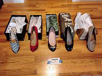 Five pairs of women's shoes in boxes, size 7, all unworn shoe pairs displayed on wooden floor including patterned heel, red velvet bow, black heel with buckle, black suede bow, and flat casual suede.