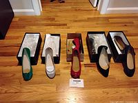 Front view of five pairs of women's size 7 shoes placed on the floor with boxes behind them, showing green suede flats, beige flats, red flats with bow, black heels, and black flats with bow.