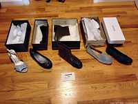 All five pairs of women's shoes arranged side by side on wooden floor, showing styles and colors, with some open boxes visible