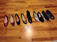 Eight pairs of women's size 7 shoes on wooden floor including flats, boots, slip-ons, sneakers, and heels in various colors and patterns.