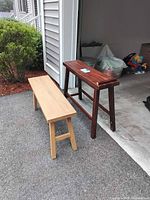 Two wood benches side by side outside a garage, one long natural light wood bench and one dark reddish wood bench