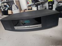 Front view of the black Bose Wave Music System showing the CD player slot, digital clock display, and speaker grille.