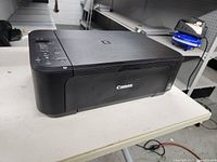 Canon Pixma all-in-one printer scanner shown from a side angle on a table, black color with top lid closed.